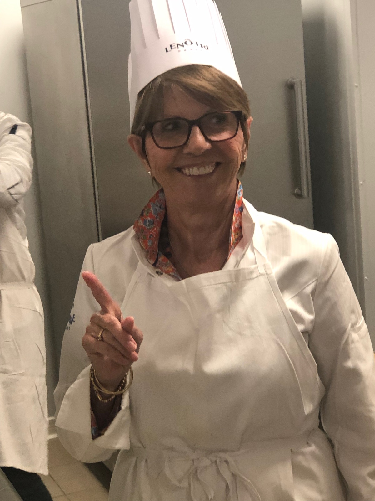A smiling woman wearing a chef hat during a cooking lesson.
